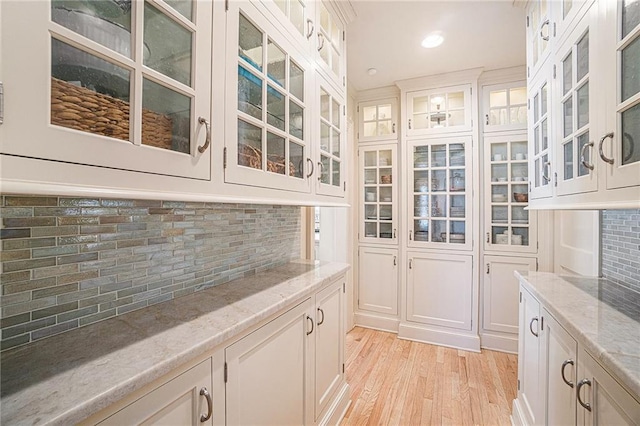 interior space featuring decorative backsplash, light stone counters, white cabinetry, and light hardwood / wood-style flooring