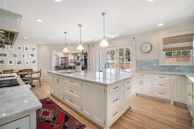 kitchen with sink, white cabinets, light stone counters, an island with sink, and hanging light fixtures