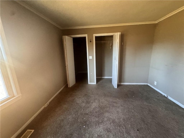 unfurnished bedroom featuring multiple closets, dark carpet, a textured ceiling, and ornamental molding