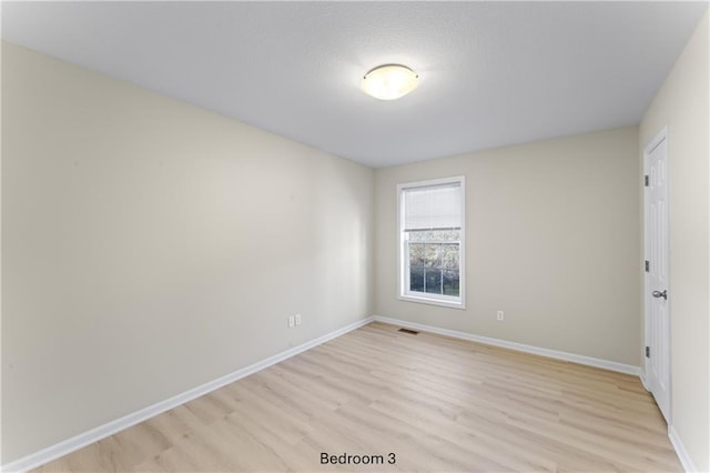 spare room featuring visible vents, light wood-style flooring, and baseboards