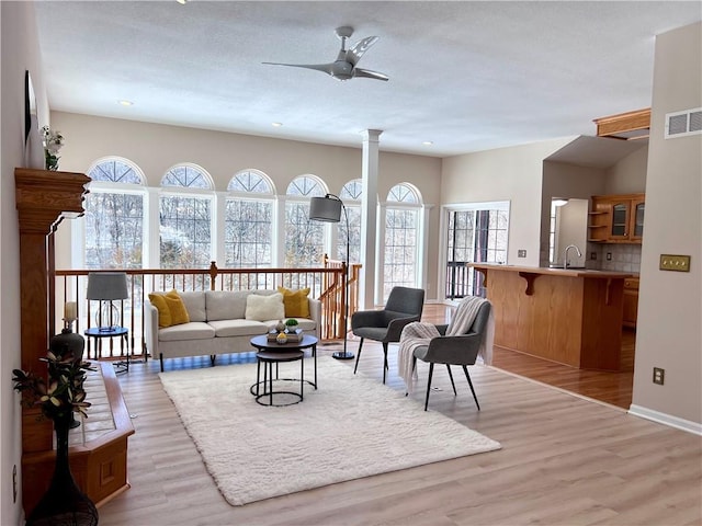 living room featuring ornate columns, visible vents, light wood-style flooring, ceiling fan, and baseboards