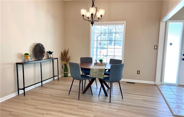 dining space with light wood-type flooring, baseboards, and a notable chandelier