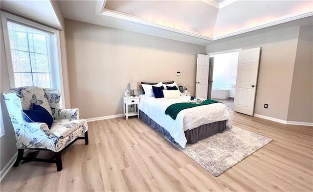 bedroom with a tray ceiling, light wood-type flooring, and baseboards