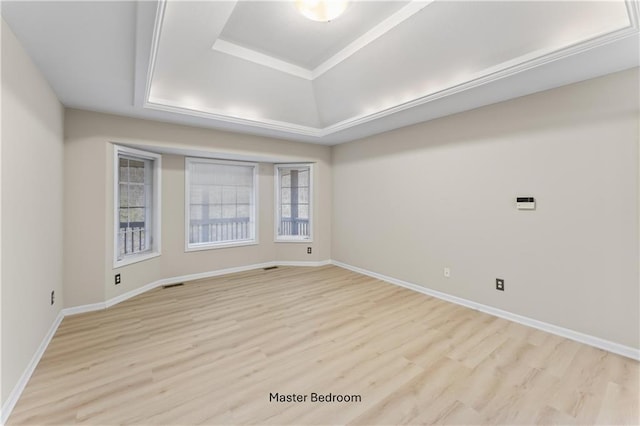 unfurnished room with light wood finished floors, baseboards, visible vents, and a raised ceiling