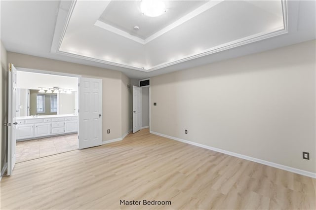 unfurnished bedroom featuring light wood finished floors, a tray ceiling, baseboards, and ensuite bathroom