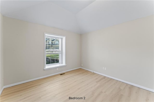 unfurnished room featuring light wood-type flooring, visible vents, vaulted ceiling, and baseboards