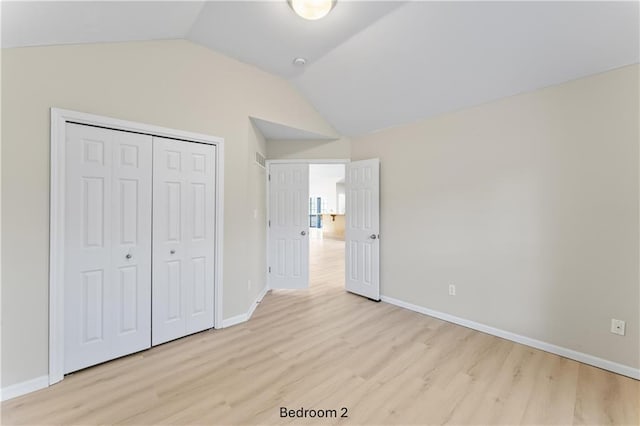 unfurnished bedroom featuring lofted ceiling, a closet, baseboards, and light wood finished floors