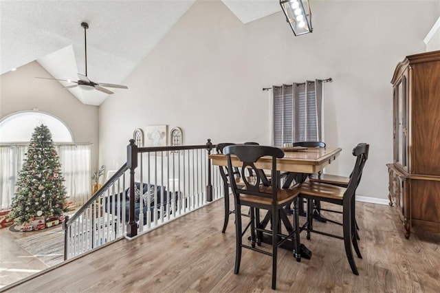 dining space with hardwood / wood-style floors, high vaulted ceiling, and ceiling fan