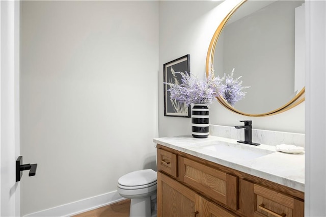 half bath with vanity, toilet, baseboards, and wood finished floors