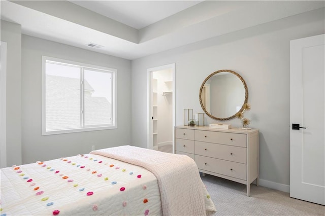 bedroom with light carpet, baseboards, a raised ceiling, and a walk in closet