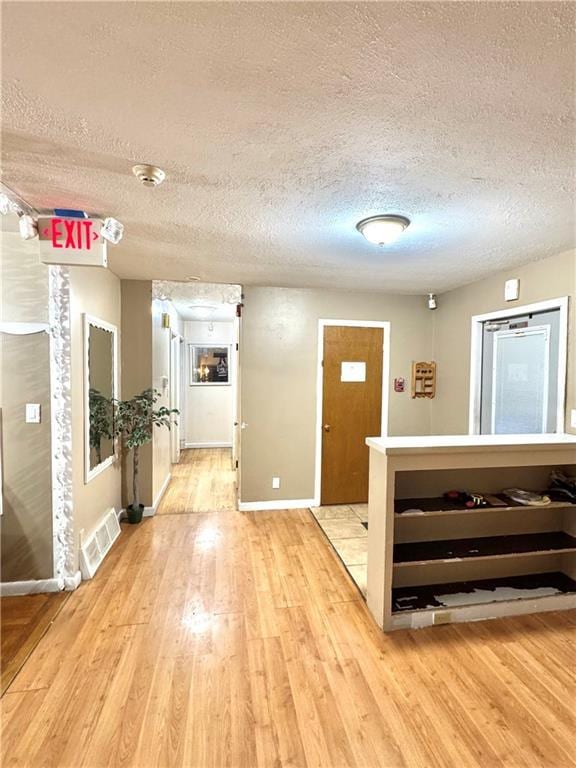 hallway with baseboards, visible vents, a textured ceiling, and light wood finished floors