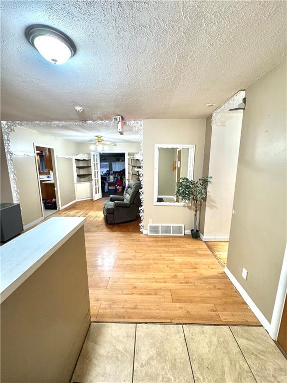 hallway with baseboards, a textured ceiling, visible vents, and wood finished floors