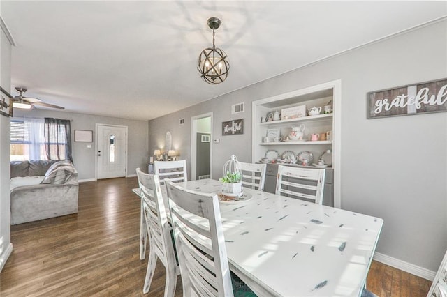 dining space featuring built in shelves, ceiling fan with notable chandelier, and dark wood-type flooring