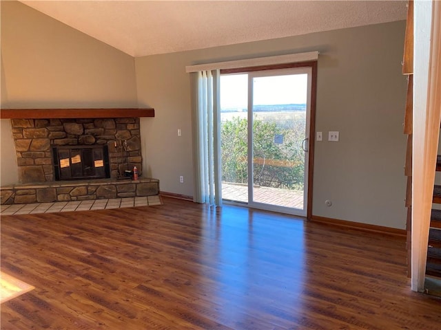 unfurnished living room featuring a stone fireplace, dark hardwood / wood-style flooring, a textured ceiling, and vaulted ceiling