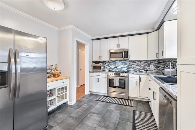 kitchen featuring stainless steel appliances, tasteful backsplash, ornamental molding, white cabinets, and light stone counters