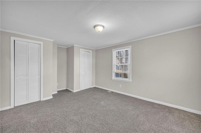 unfurnished bedroom featuring a textured ceiling, carpet, two closets, and ornamental molding