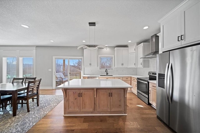 kitchen featuring a center island, wall chimney exhaust hood, stainless steel appliances, pendant lighting, and white cabinets