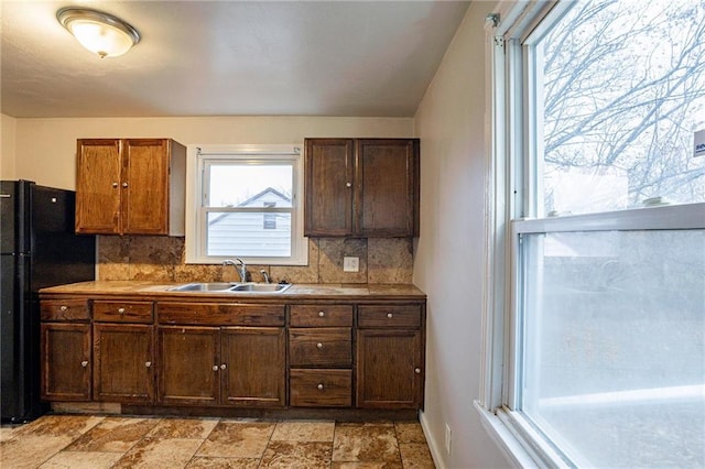 kitchen with decorative backsplash, black refrigerator, and sink