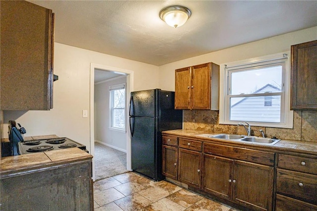 kitchen with stove, black refrigerator, sink, decorative backsplash, and tile counters