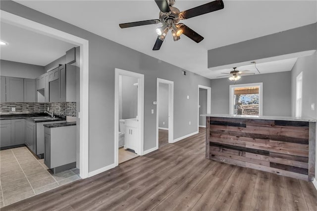 kitchen featuring sink, decorative backsplash, gray cabinets, ceiling fan, and wood-type flooring