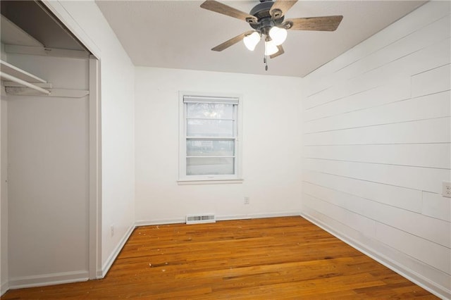 unfurnished bedroom with hardwood / wood-style flooring, ceiling fan, a closet, and wood walls