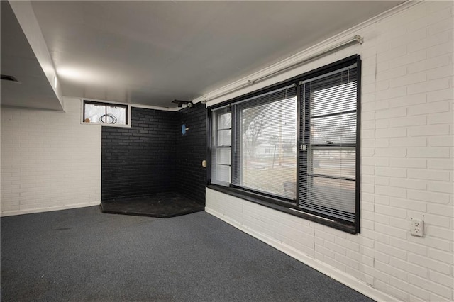 basement featuring carpet floors, crown molding, a wealth of natural light, and brick wall