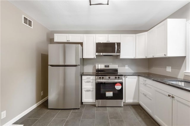 kitchen featuring sink, dark stone countertops, white cabinets, dark tile patterned flooring, and stainless steel appliances