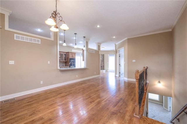 unfurnished living room featuring crown molding, hardwood / wood-style floors, and a notable chandelier