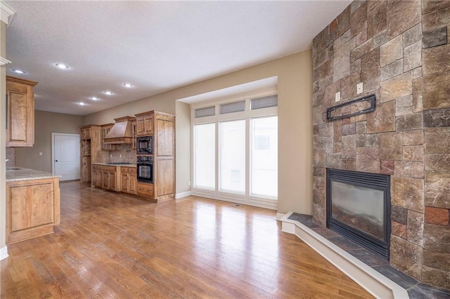 kitchen featuring a fireplace, wood-type flooring, custom exhaust hood, black appliances, and light stone countertops