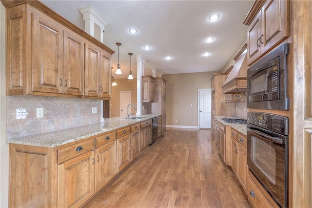 kitchen with sink, premium range hood, hanging light fixtures, light stone counters, and black appliances