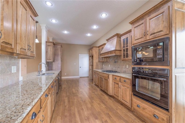 kitchen featuring premium range hood, decorative light fixtures, sink, black appliances, and light stone countertops