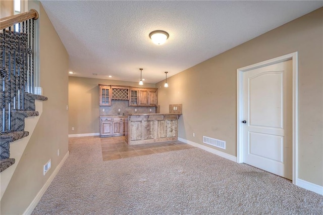 kitchen featuring tasteful backsplash, a textured ceiling, kitchen peninsula, pendant lighting, and light colored carpet