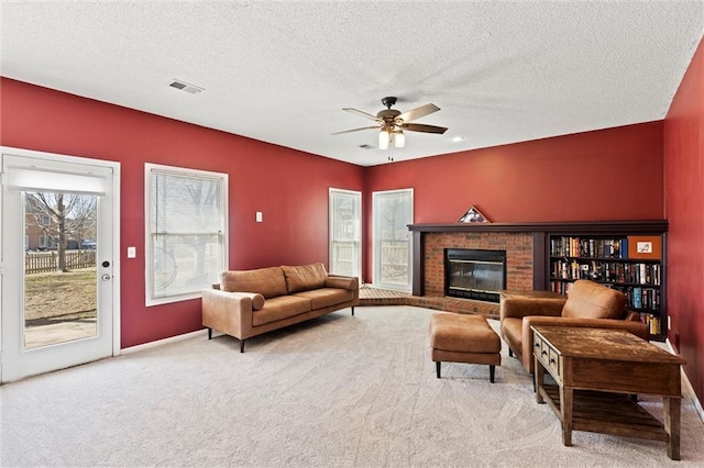 living area featuring ceiling fan, a textured ceiling, a brick fireplace, and carpet flooring