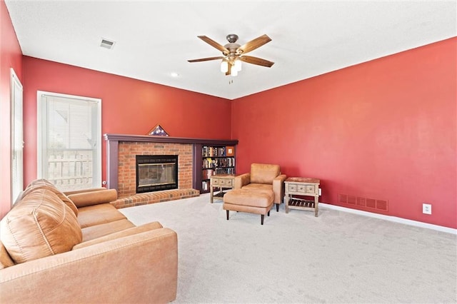 carpeted living area with ceiling fan, a brick fireplace, visible vents, and baseboards