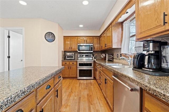 kitchen featuring brown cabinets, stainless steel appliances, tasteful backsplash, light wood-style floors, and a sink