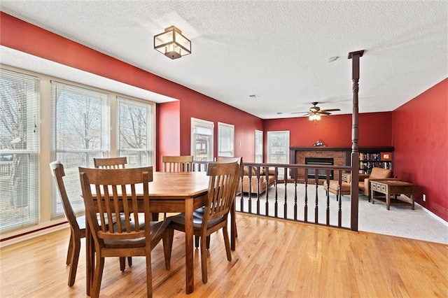 dining area featuring a brick fireplace, ceiling fan, light wood-style flooring, and a textured ceiling