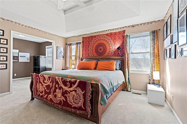 carpeted bedroom featuring a textured ceiling, a raised ceiling, visible vents, and baseboards