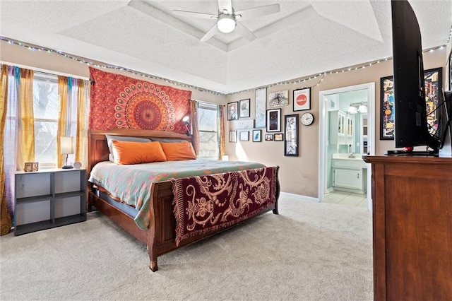 carpeted bedroom with baseboards, a raised ceiling, a ceiling fan, ensuite bath, and a textured ceiling