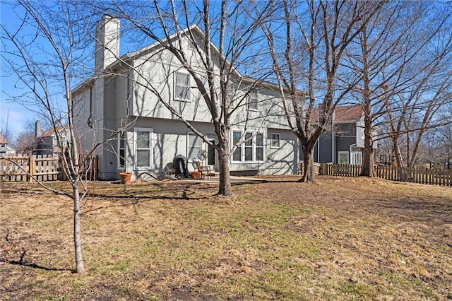 rear view of house with a chimney, fence, and a yard