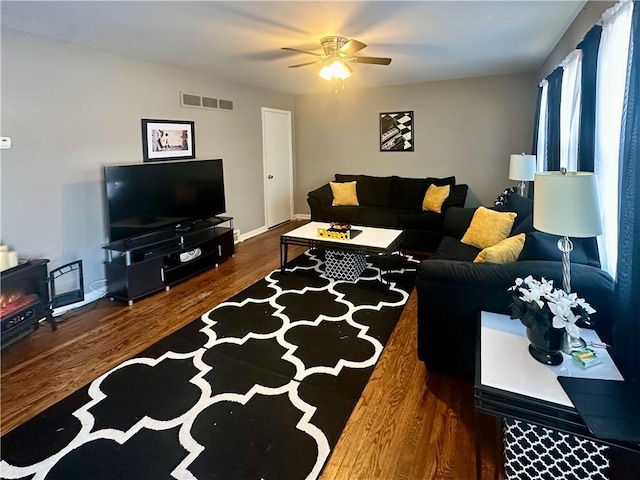 living room with dark wood-type flooring, ceiling fan, and a wood stove