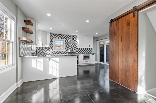 kitchen featuring white cabinets, decorative backsplash, a barn door, and exhaust hood