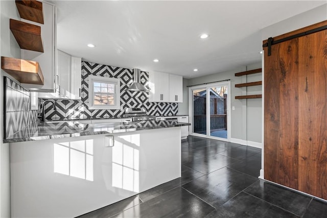 kitchen with a healthy amount of sunlight, a barn door, white cabinetry, and dark stone counters