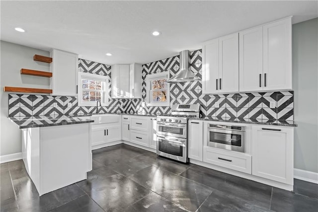 kitchen with white cabinets, appliances with stainless steel finishes, decorative backsplash, and wall chimney range hood