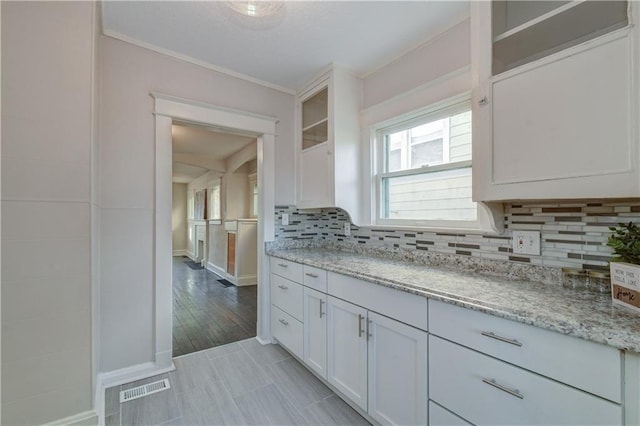 kitchen with white cabinets, backsplash, light hardwood / wood-style floors, and light stone countertops