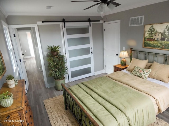 bedroom featuring hardwood / wood-style floors, a barn door, ceiling fan, and crown molding