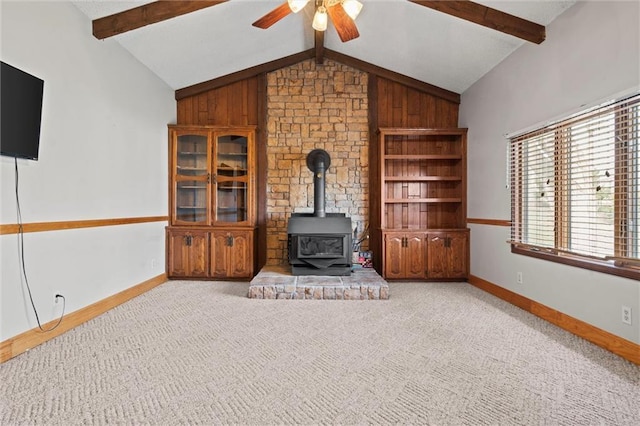 carpeted living area featuring vaulted ceiling with beams, ceiling fan, a wood stove, and baseboards