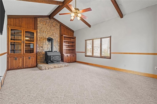 unfurnished living room featuring vaulted ceiling with beams, ceiling fan, light carpet, and a wood stove