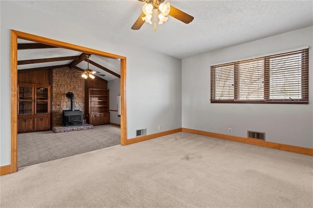 unfurnished living room featuring a wood stove, carpet floors, visible vents, and a textured ceiling