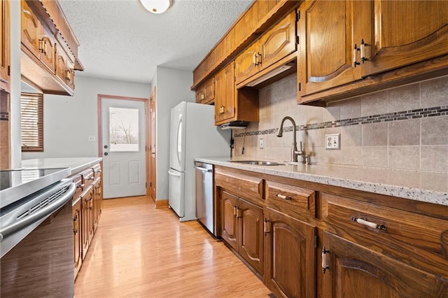 kitchen with brown cabinets, stainless steel appliances, tasteful backsplash, a sink, and light wood-type flooring