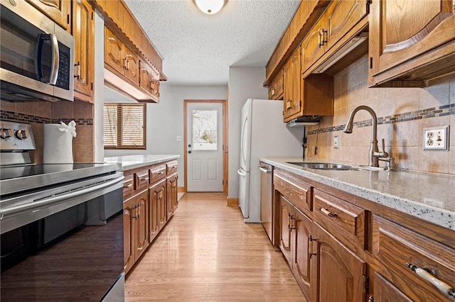 kitchen featuring brown cabinets, stainless steel appliances, decorative backsplash, a sink, and light wood-type flooring